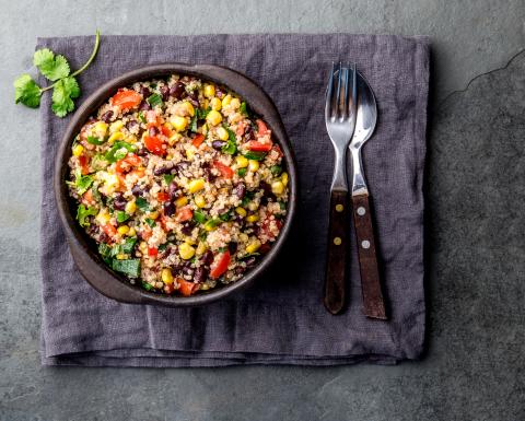 Quinoa and Greens in a bowl on a placemat with garnish and silverware.