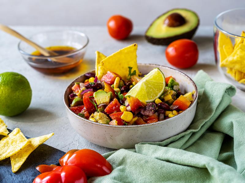 Bowl of Cowboy Caviar on a table alongside chips and vegetables