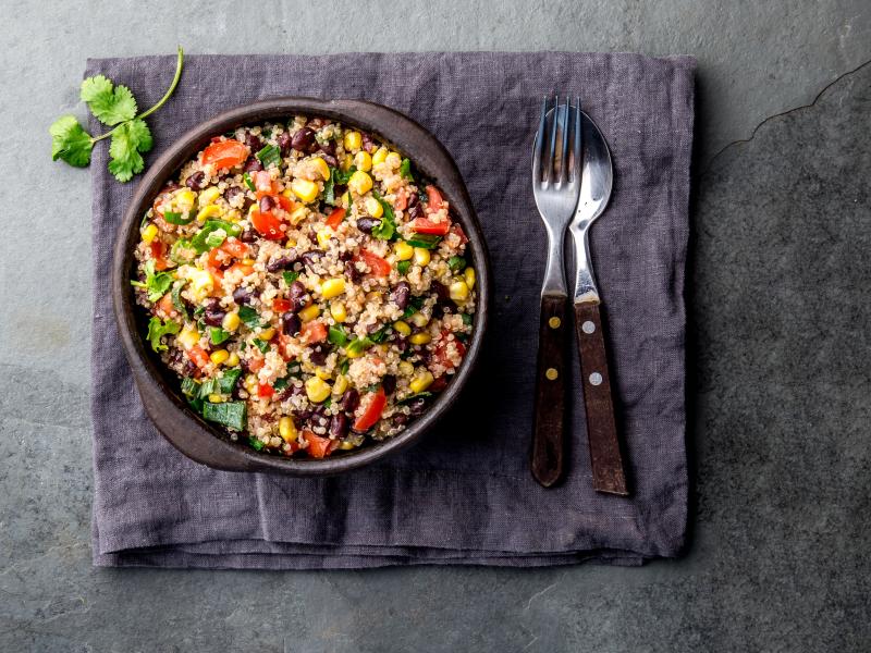 Quinoa and Greens in a bowl on a placemat with garnish and silverware.